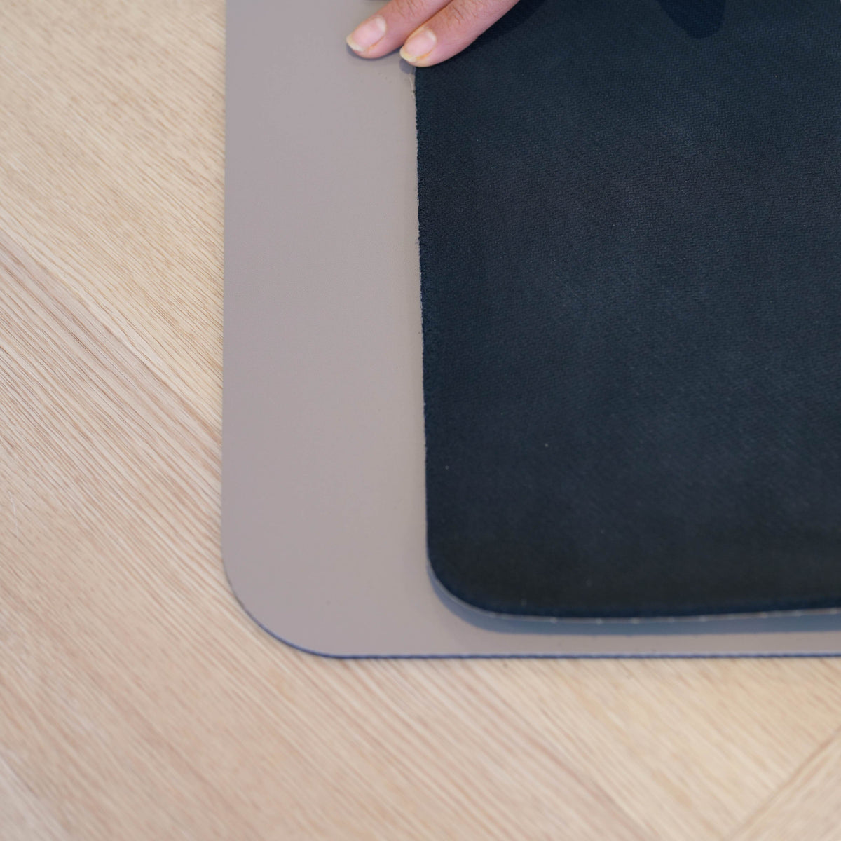 Close-up of the rounded corners of Charcoal Grey and Sandstone waterproof yoga mats on a timber floor