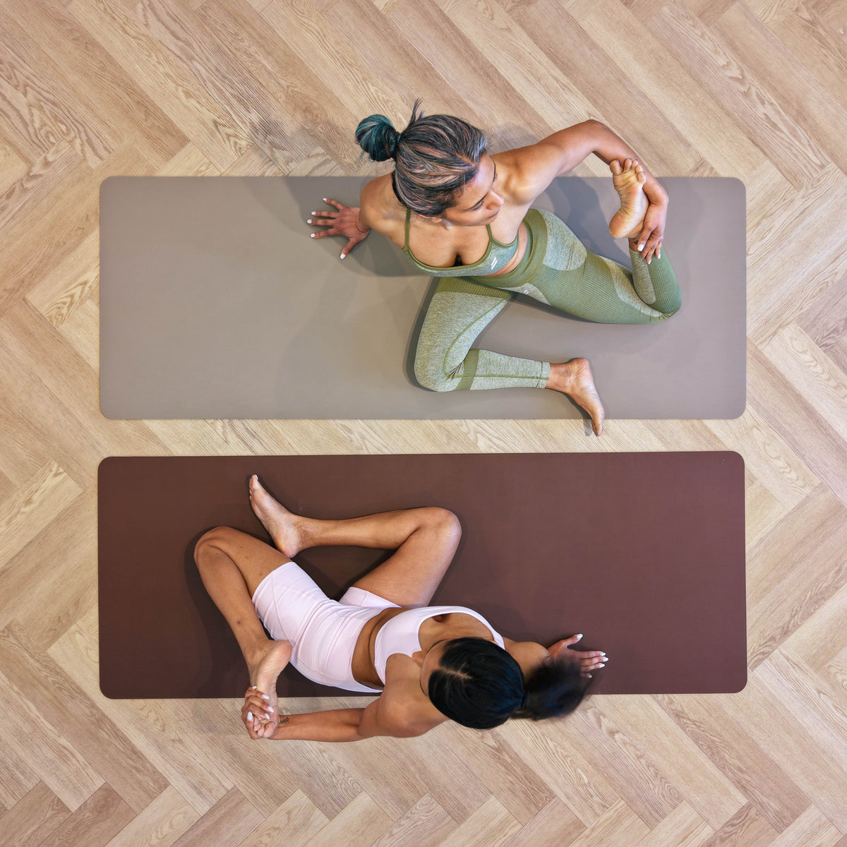Two women stretching on Sandstone and Mahogany Zenvibes waterproof vegan leather yoga mats, top view on a timber floor