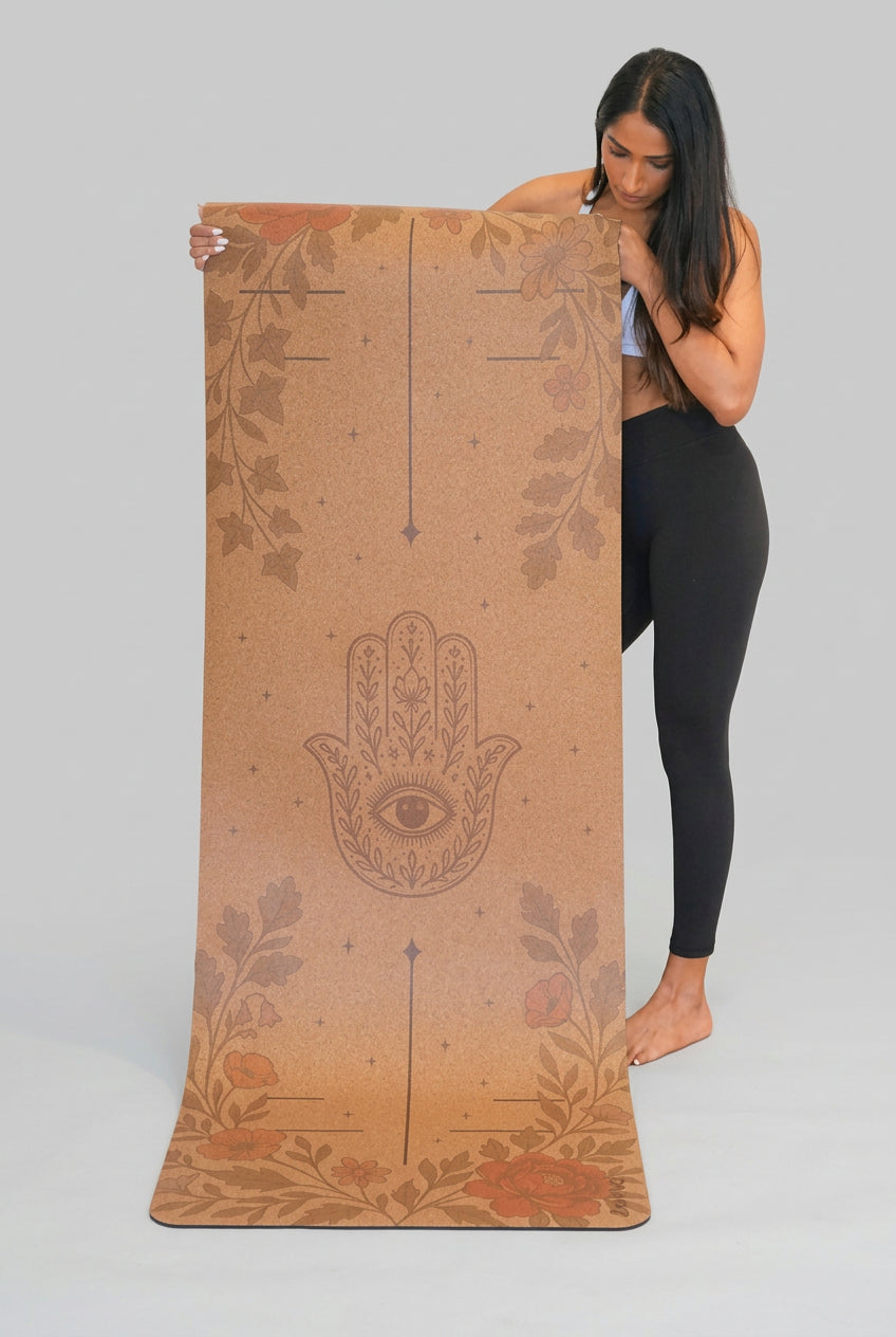 Woman holding a Zenvibes extra wide cork yoga mat with a Hamsa Harmony design.