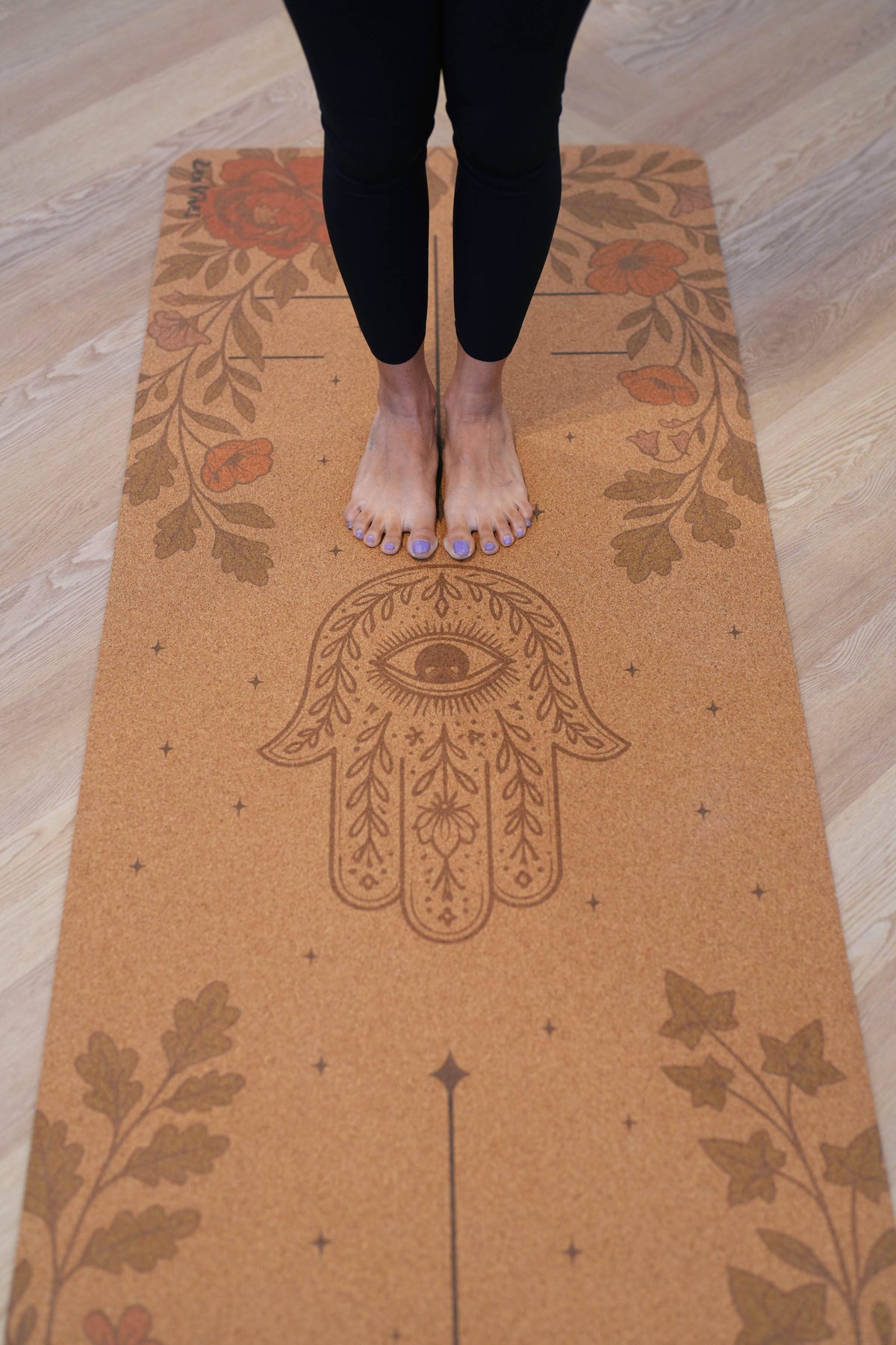 Bare feet standing on a Zenvibes Hamsa Harmony extra wide cork yoga mat with floral designs.