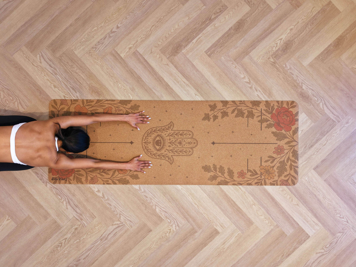 Top view of a person on a Zenvibes Hamsa Harmony extra wide cork yoga mat on a wooden floor.
