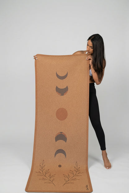 Woman holding a Zenvibes extra wide cork yoga mat with moon phase and botanical designs
