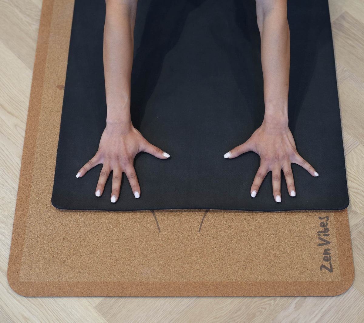 Hands resting on a Zenvibes extra wide cork yoga mat with a black non-slip surface.