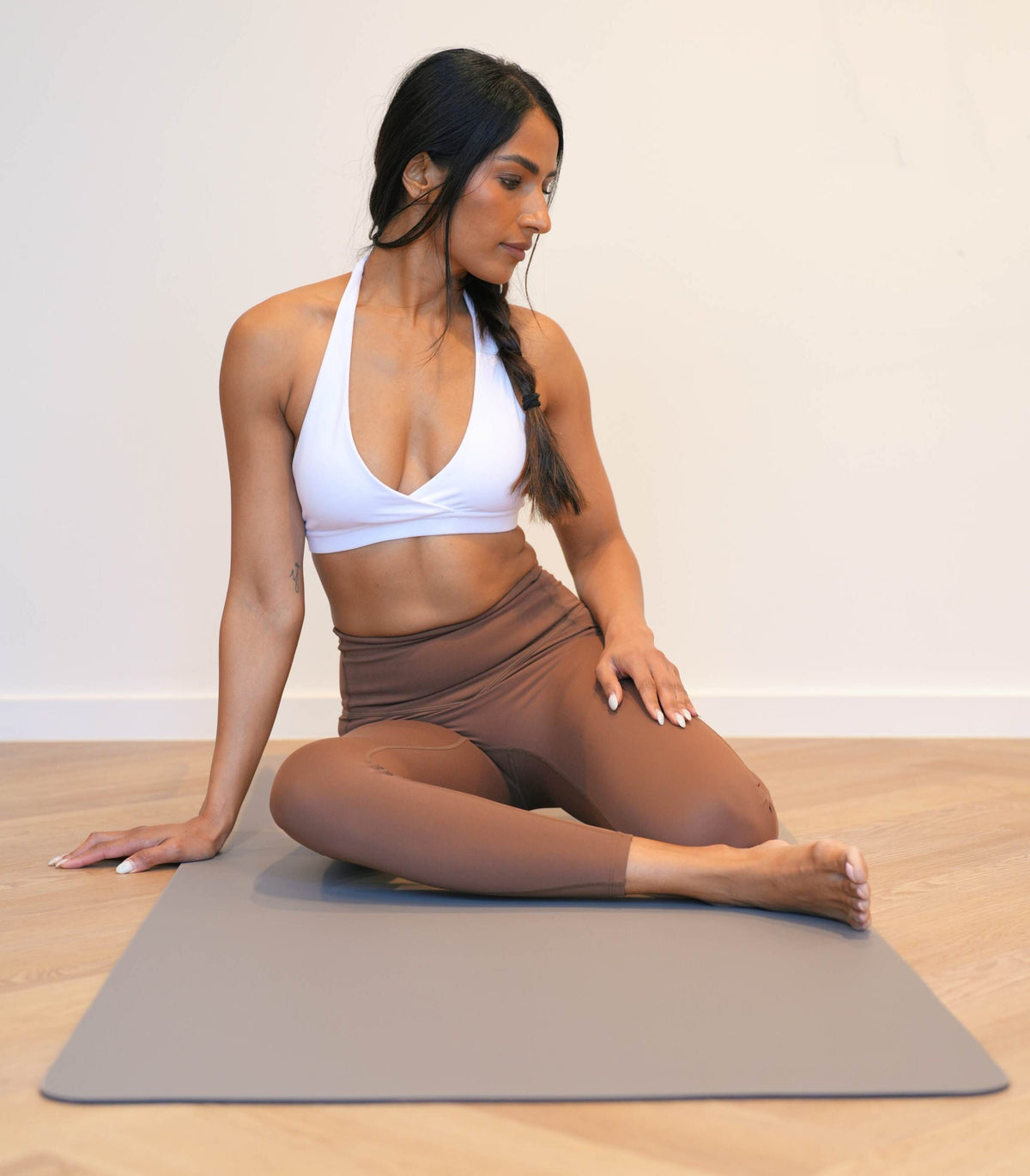 Woman sitting on a Sandstone vegan leather yoga mat on a timber floor