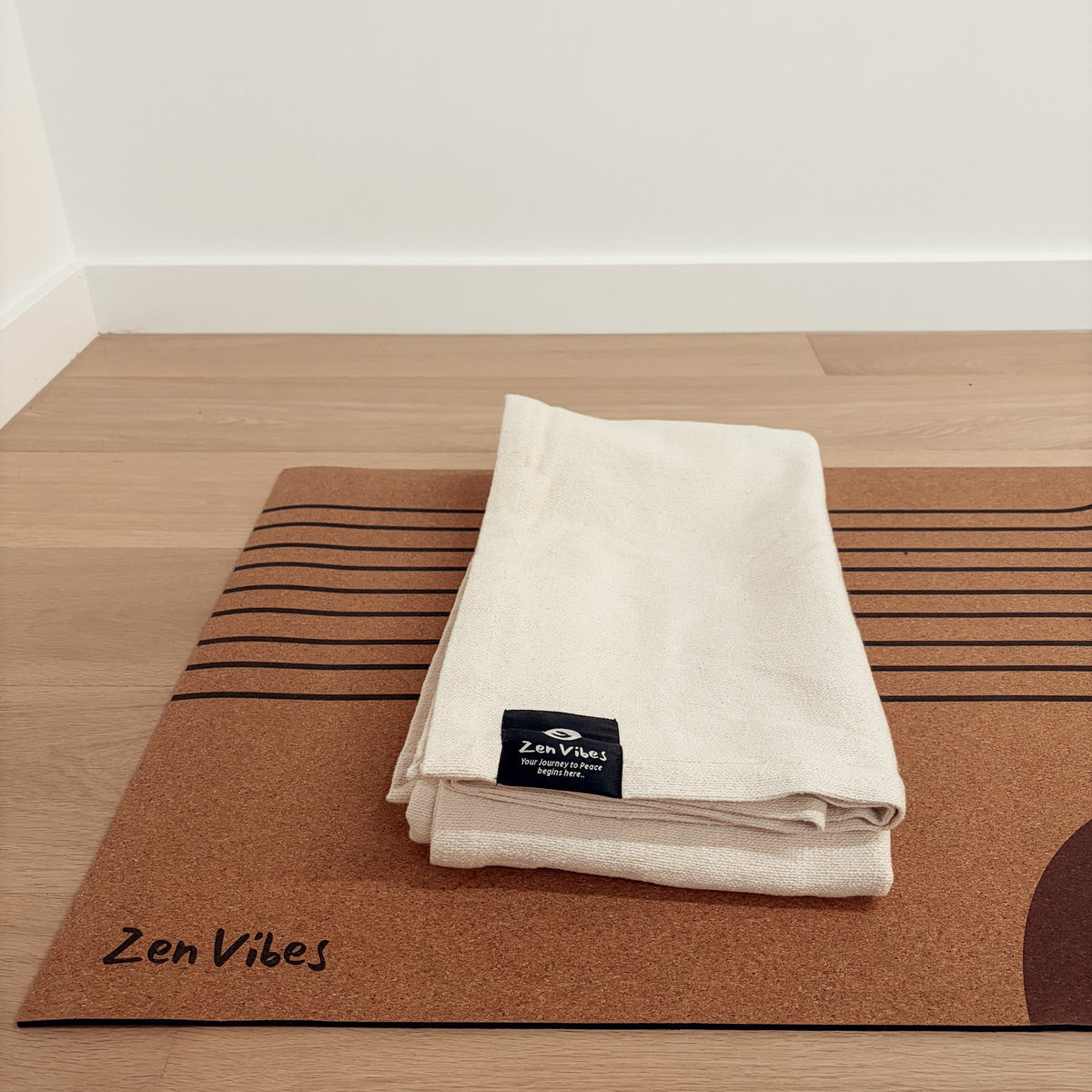 Folded cream-colored yoga towel resting on a brown cork yoga mat with Zen Vibes branding.